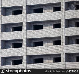 Construction site. Unfinished apartment building made of white bricks. Empty windows and balconies.
