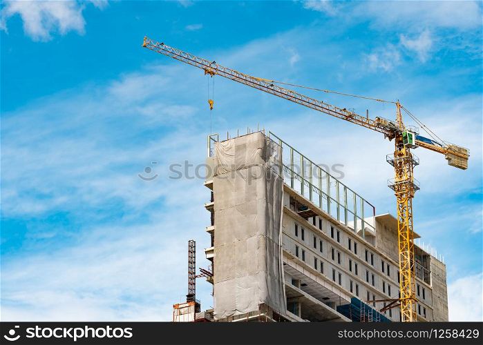 Construction site with crane and building. Real estate industry. Crane use reel lift up equipment in construction site. Building made of steel and concrete. Crane work against blue sky and white cloud