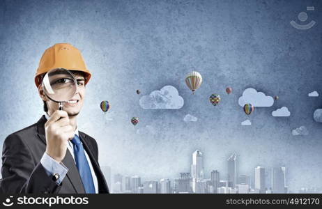 Construction strategy. Young man architect against sketch background looking in magnifying glass