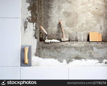 construction tools notched trowel and hammer on tiles mortar wall