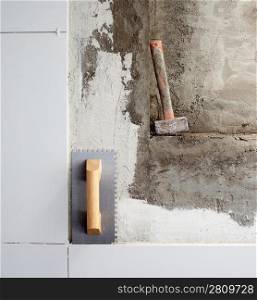 construction tools notched trowel and hammer on tiles mortar wall