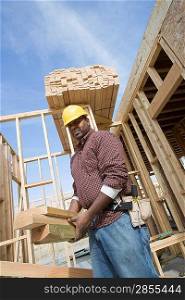 Construction worker carrying wooden plank