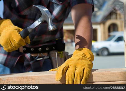 Construction worker hammering nail to wooden plank on construction site