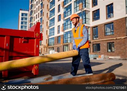 Construction worker holding pipe on site outdoors. Residential house apartment building area. Construction worker holding pipe on site outdoors
