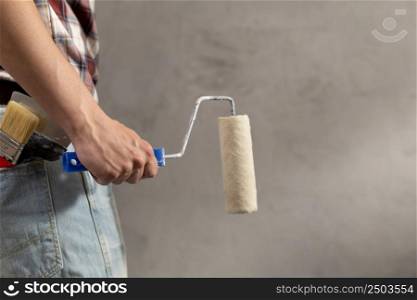 Construction worker man holding paint roller tool in house room renovation. Male hand and construction tools near concrete or plaster wall. Home renovation concept