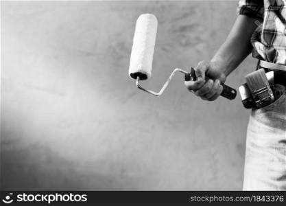 Construction worker man holding paint roller tool near concrete or plaster wall. Male hand and construction tools for house room renovation. Home renovation concept