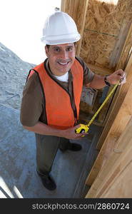 Construction worker measuring wall with measure taper inside half constructed house