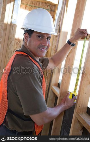 Construction worker measuring wall with measure taper inside half constructed house