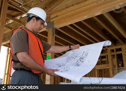 Construction worker observing half constructed house while holding blueprints