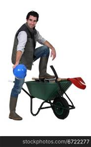 Construction worker showing off his hard hat, wheelbarrow and tools