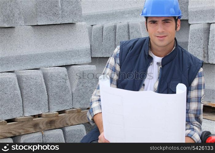 Construction worker standing next to pallets of concrete curb while looking at some plans