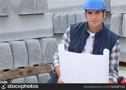 Construction worker standing next to pallets of concrete curb while looking at some plans