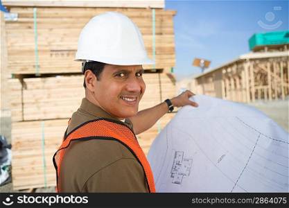 Construction worker standing on construction site and holding blueprints