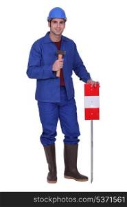 Construction worker standing with a mallet and traffic sign