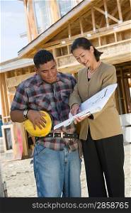 Construction worker studying blueprint with surveyor