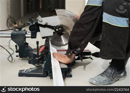 Construction worker uses a portable circular saw to cut a styrofoam baseboard. Circular saw with a sharp rotating blade, new baseboard, woodworking machinery, equipment