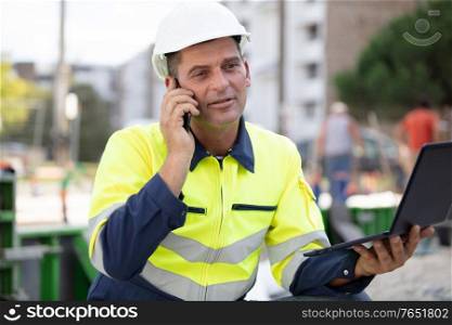 construction worker using laptop and talking on smartphone