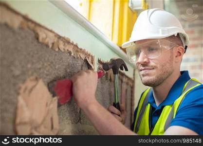 Construction Worker With Chisel Removing Plaster From Wall In Renovated House