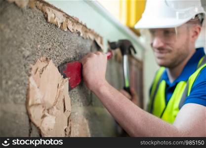 Construction Worker With Chisel Removing Plaster From Wall In Renovated House