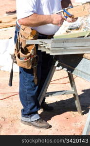 Construction worker with tool belt works with a clamp by a sawhorse.