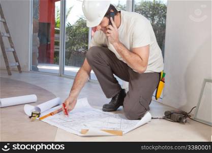 Construction worker working on blueprint and talking on cellphone