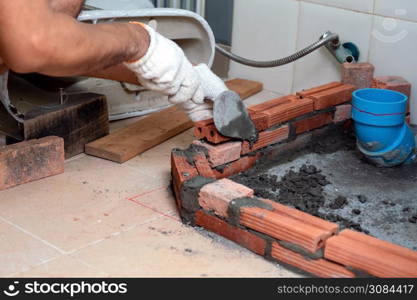 Construction workers are laying red bricks around the sewer in the bathroom.