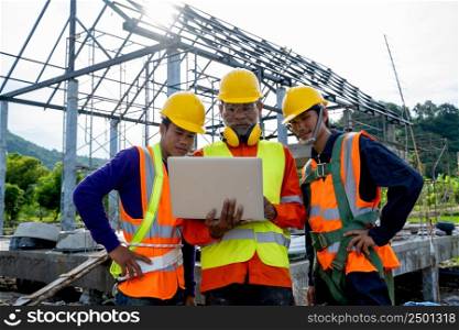 Construction workers wearing safety clothing and discussing on construction site checking office laptop at construction site.