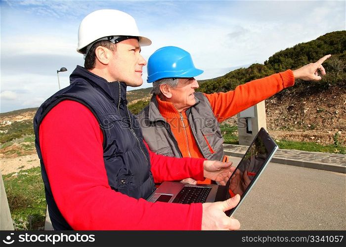 Construction workers with laptop computer looking at building