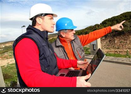 Construction workers with laptop computer looking at building