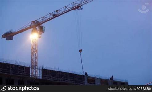 Construction works in the evening: crane moving without cargo. Snowing