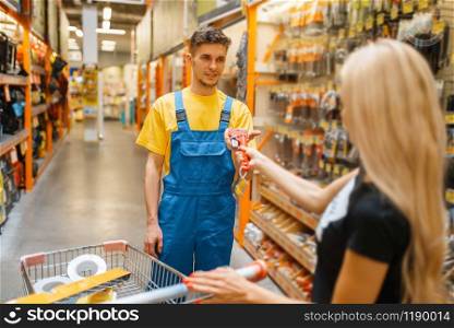 Consultant and female purchaser in hardware store. Seller in uniform and woman in diy shop, shopping in building supermarket