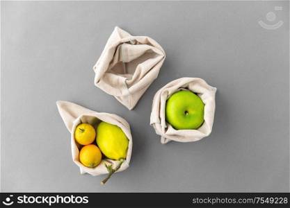 consumerism and eco friendly concept - fruits in reusable canvas bags for food shopping s on grey background. fruits in reusable canvas bags for food shopping