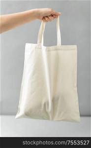 consumerism and eco friendly concept - hand holding reusable canvas bag for food shopping on grey background. hand holding reusable canvas bag for food shopping