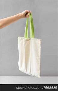 consumerism and eco friendly concept - hand holding reusable canvas bag for food shopping on grey background. hand holding reusable canvas bag for food shopping