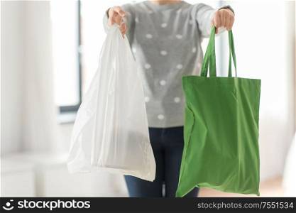 consumerism and eco friendly concept - woman holding reusable canvas tote for food shopping and plastic bag on grey background. woman with tote for shopping and plastic bag