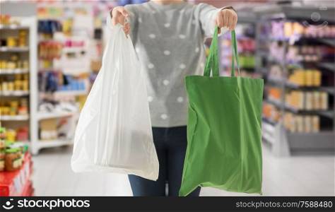 consumerism and eco friendly concept - woman holding reusable canvas tote for food shopping and plastic bag over supermarket on background. woman with tote for shopping and plastic bag