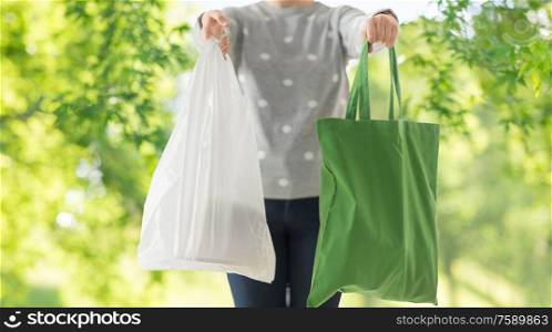 consumerism and eco friendly concept - woman holding reusable canvas tote for food shopping and plastic bag over green natural background. woman with tote for shopping and plastic bag