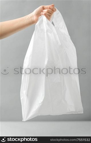 consumerism and eco friendly concept - woman holding white disposable plastic bag over grey background. woman holding white disposable plastic bag