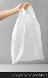consumerism and eco friendly concept - woman holding white disposable plastic bag over grey background. woman holding white disposable plastic bag