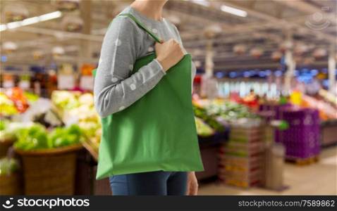 consumerism and eco friendly concept - woman with green reusable canvas bag for food shopping over supermarket on background. woman with reusable canvas bag for food shopping