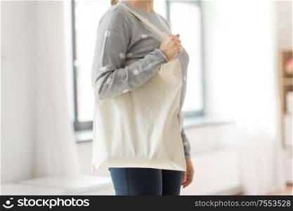 consumerism and eco friendly concept - woman with white reusable canvas bag for food shopping on grey background. woman with reusable canvas bag for food shopping