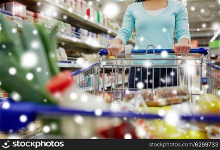 consumerism and people concept - female customer with shopping cart or trolley buying food at grocery store or supermarket over snow. customer with food in shopping cart at supermarket
