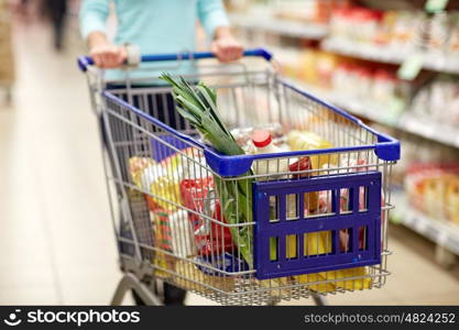 consumerism and people concept - woman with shopping cart or trolley buying food at grocery store or supermarket. woman with food in shopping cart at supermarket