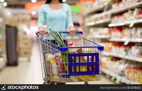 consumerism and people concept - woman with shopping cart or trolley buying food at grocery store or supermarket. woman with food in shopping cart at supermarket