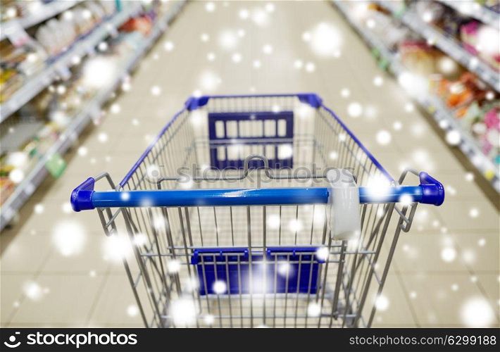 consumerism concept - empty shopping cart or trolley at supermarket over snow. empty shopping cart or trolley at supermarket