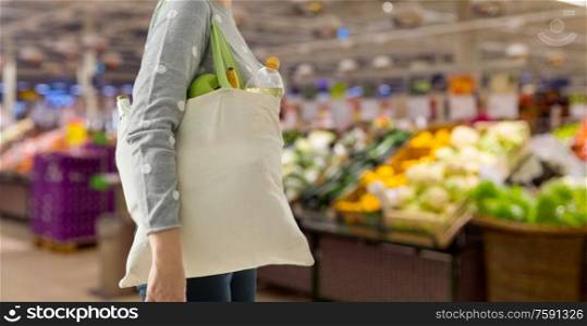 consumerism, eating and eco friendly concept - woman with white reusable canvas bag for food shopping over supermarket on background. woman with reusable canvas bag for food shopping