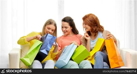 consumerism, friendship and lifestyle concept - three smiling teenage girls or friends with shopping bags at home. teenage girls with shopping bags at home