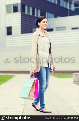consumerism, leisure and people concept - smiling woman with shopping bags coming from sale in park