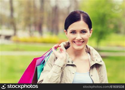 consumerism, leisure and people concept - smiling woman with shopping bags coming from sale in park