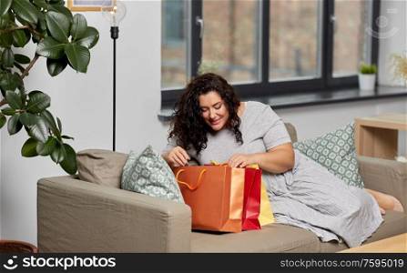 consumerism, people and sale concept - happy smiling young woman with shopping bags on sofa at home. happy young woman with shopping bags at home
